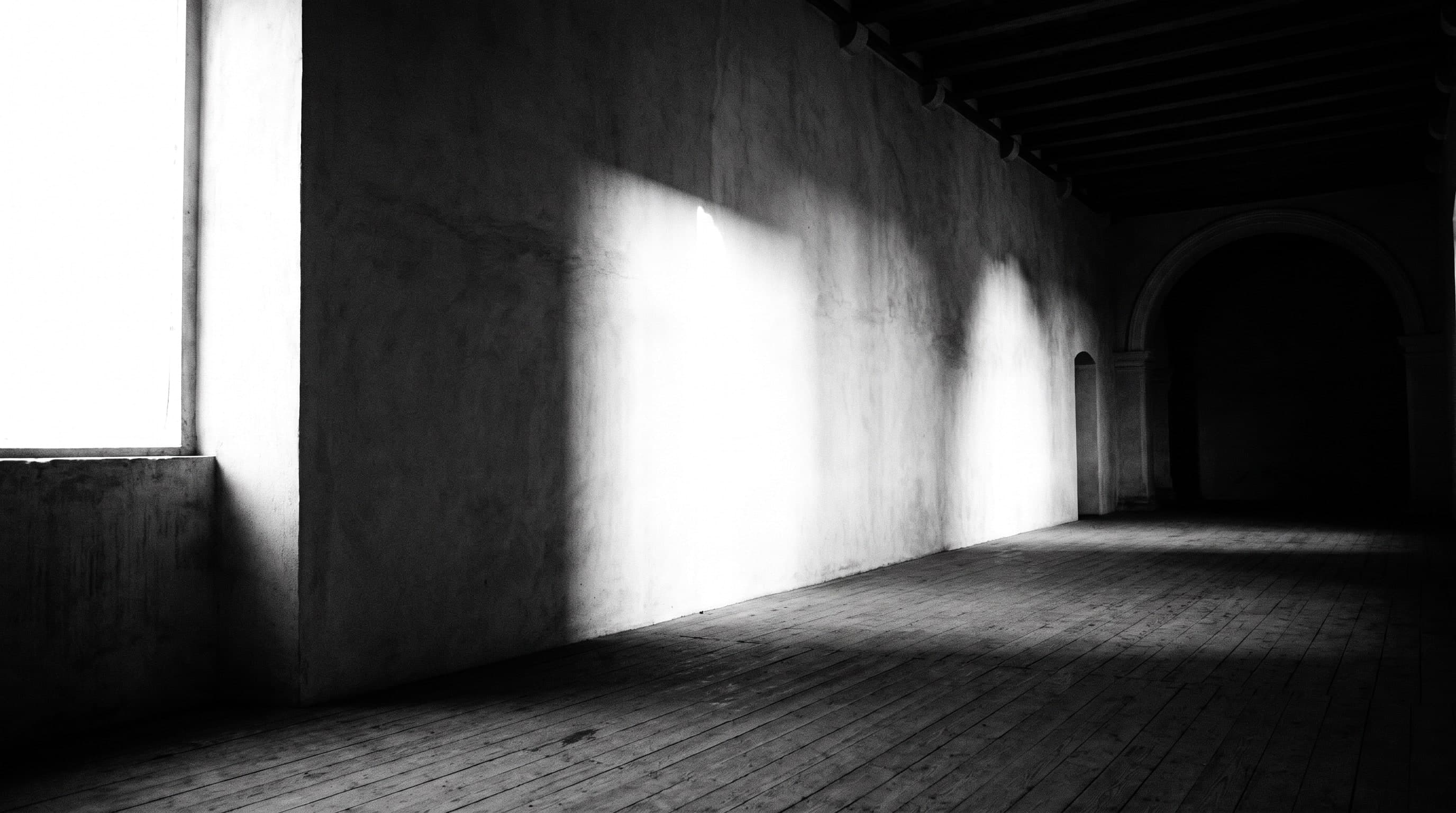 Leere weisse Wand in einem hohen Saal, ein harter Lichtbalken fällt von links über den Putz